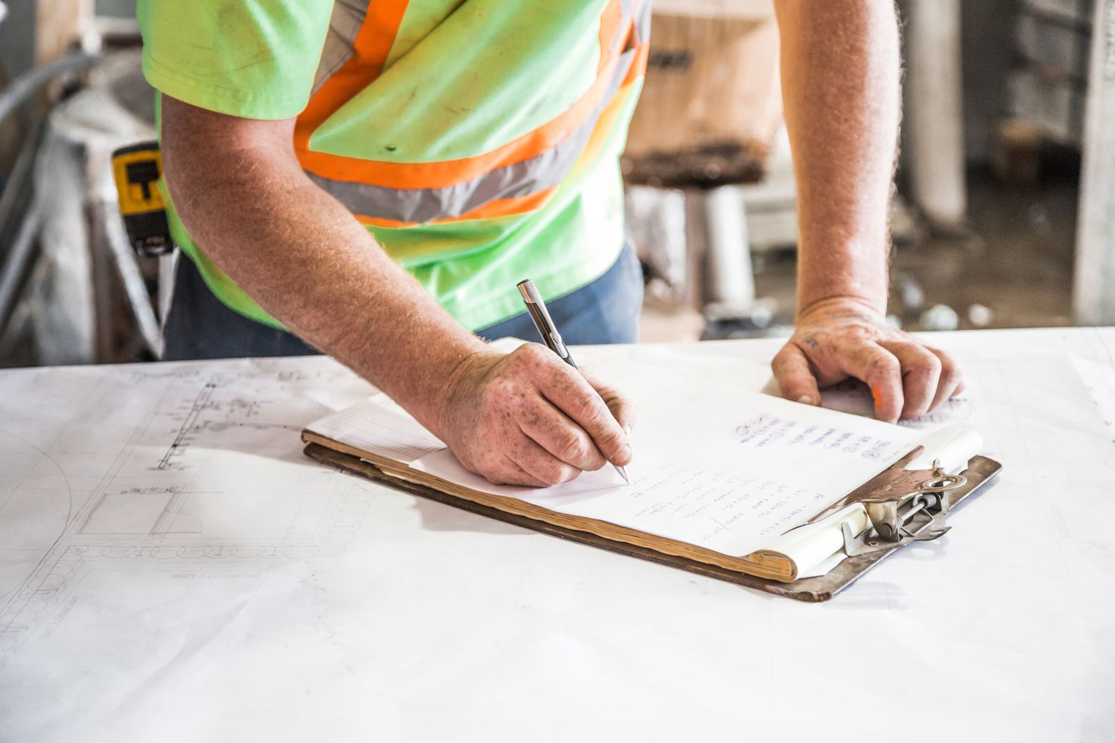 A worker in a hi-vis vest filling out a form on a clipboard at a job site table